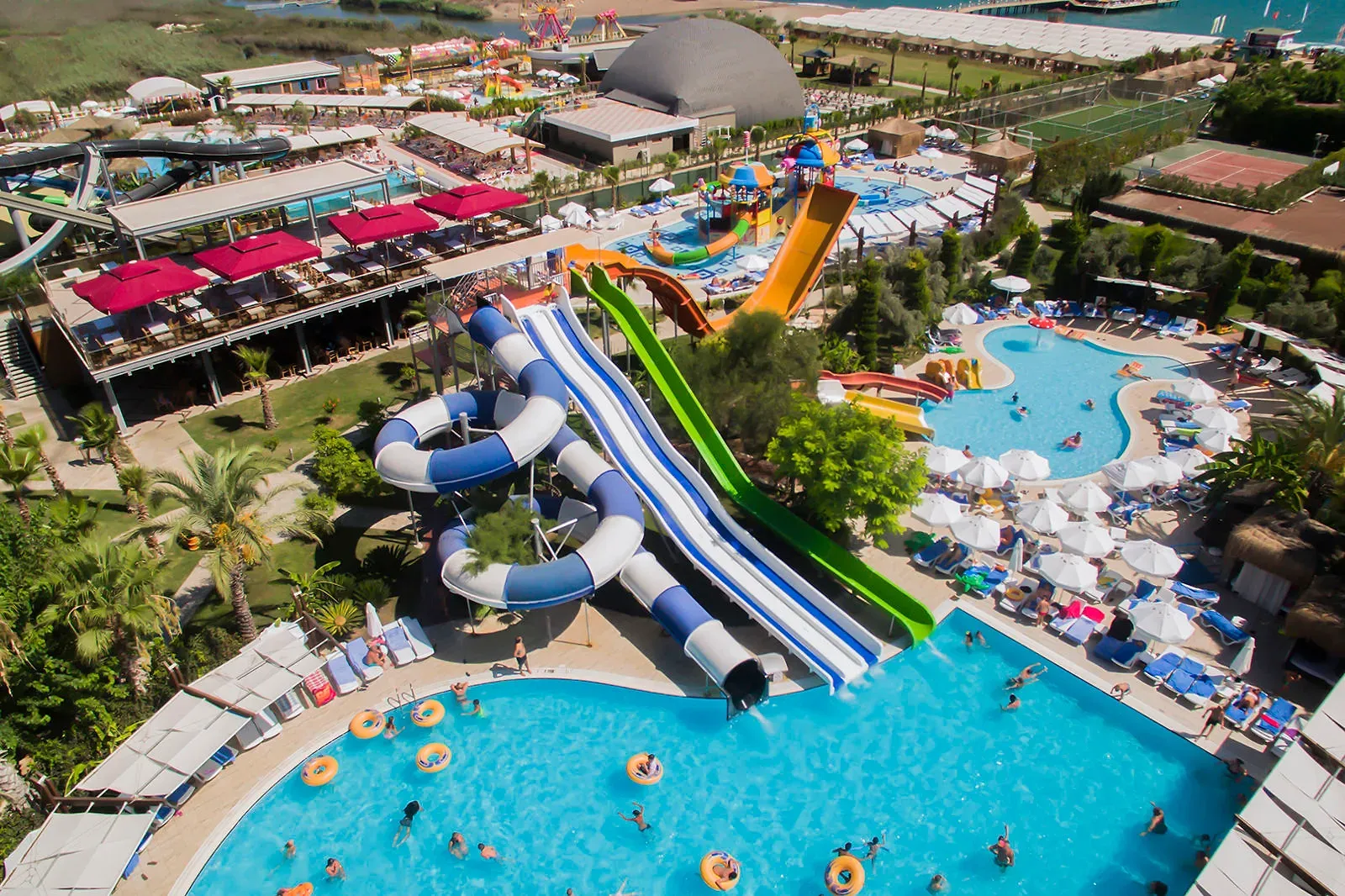 Luchtfoto van de kronkelende glijbanen boven een groot zwembad met zwemmers bij Saturn Palace Resort